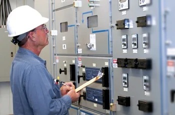 Worker in a white hard hat inspecting equipment on a wall.